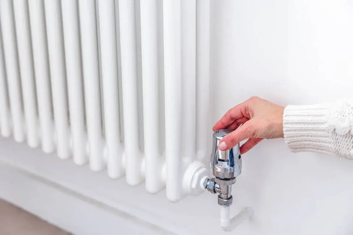Mano ajustando el termostato de un radiador blanco, quizás para entender porque suenan los radiadores.