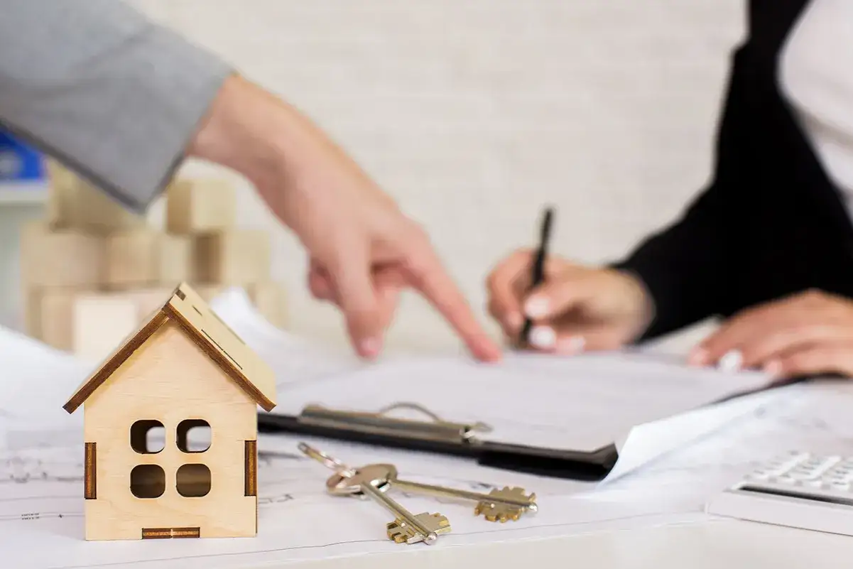 Manos firmando un contrato, llaves y casa de madera. Un ejemplo de cómo echar a un inquilino sin contrato.