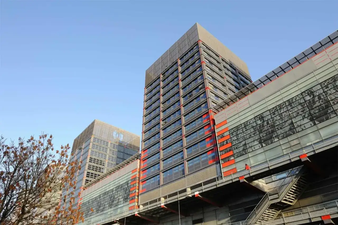 Edificios modernos con fachadas de cristal y detalles naranjas, como el studea novalille. Un árbol seco en primer plano.