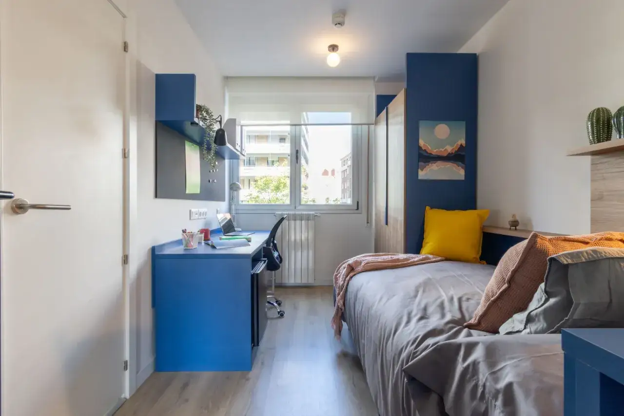 Habitación moderna en residencia laboure con cama, escritorio azul y ventana luminosa.