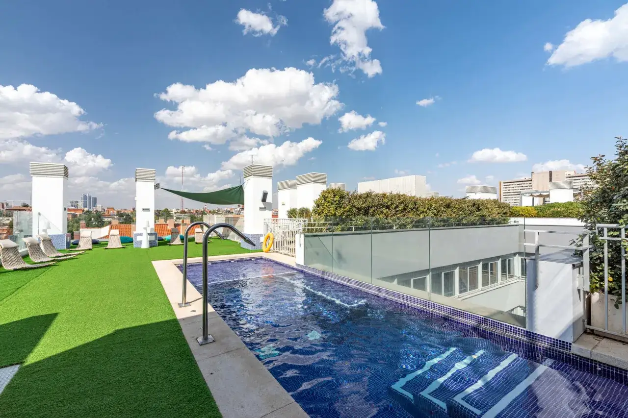 Piscina en terraza con césped artificial y tumbonas. Vista urbana de Madrid desde la resa Claudio Coello.