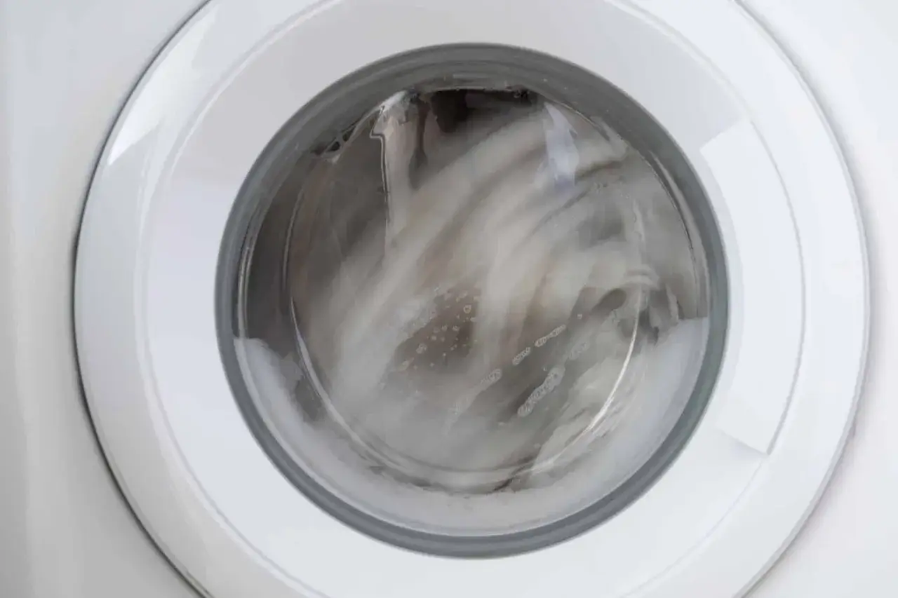 Interior de una lavadora en pleno centrifugado, con la ropa y la espuma moviéndose rápidamente.
