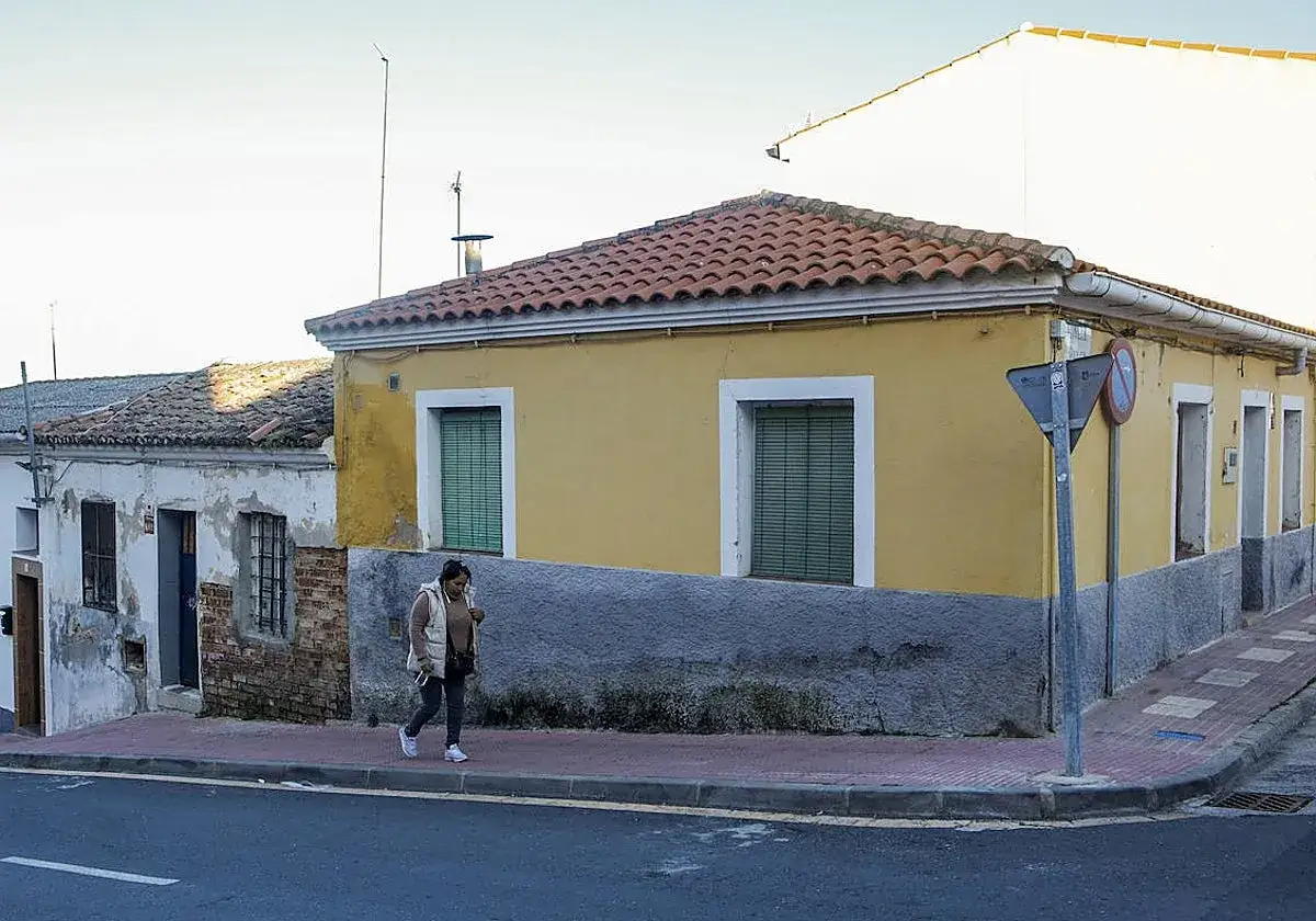 Una mujer camina por la acera frente a casas humildes. La escena evoca la precariedad y la posibilidad de un desahucio.