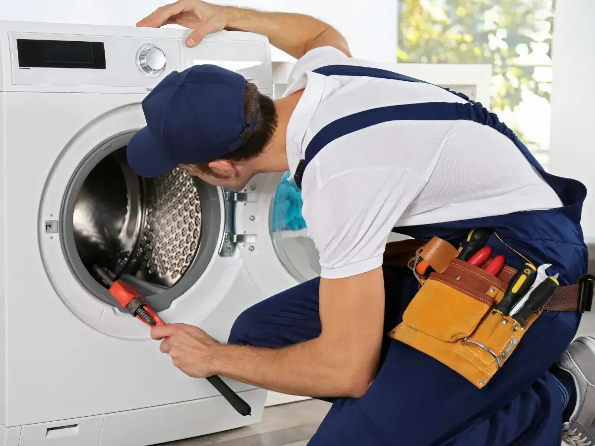Técnico revisa lavadora que hace mucho ruido al centrifugar. Usa llave inglesa y tiene cinturón de herramientas.