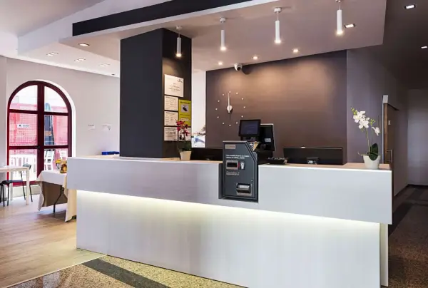 Recepción moderna y luminosa de la residencia Nuevo Versalles, con mostrador blanco, pantalla y máquina de efectivo.