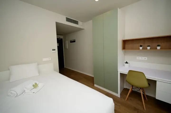 Habitación moderna con cama, armario verde y escritorio. Un espacio acogedor en Xior The Lofttown, listo para tu estancia.