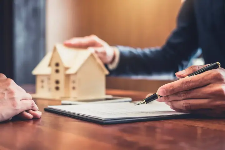 Firma de contrato de alquiler, con una maqueta de casa y un bolígrafo. Podría ser el inicio de un desahucio por precario si no se cumplen los términos.