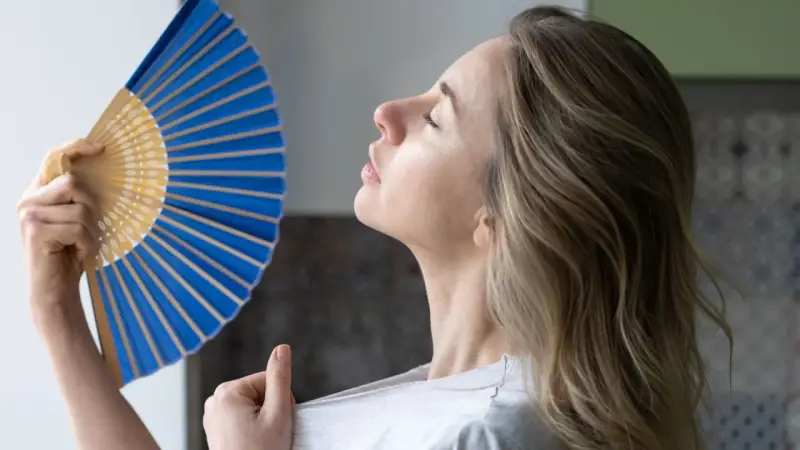 Mujer abanicándose para refrescarse, una solución para como ventilar una habitación sin ventana y combatir el calor.